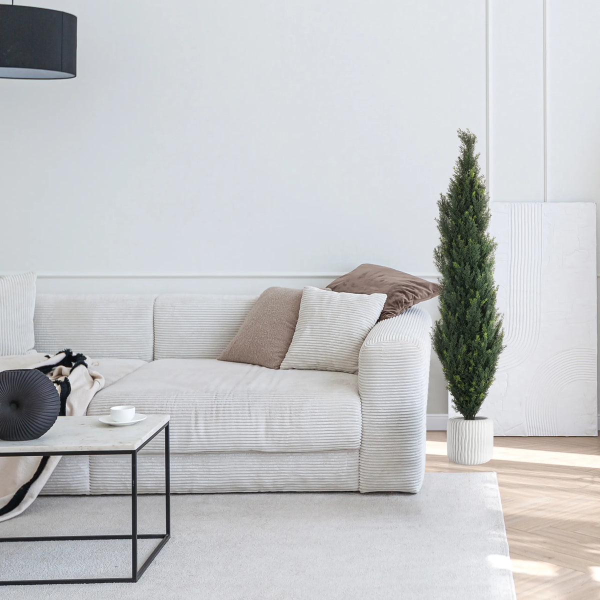 Grön konstgjord växt CEDRUS i en vit kruka bredvid en vit soffa från hjh OFFICE