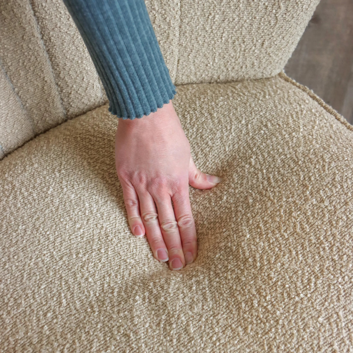 Beige strukturtyg på MANISO loungefåtölj med en hand på sitsen från hjh LIVING