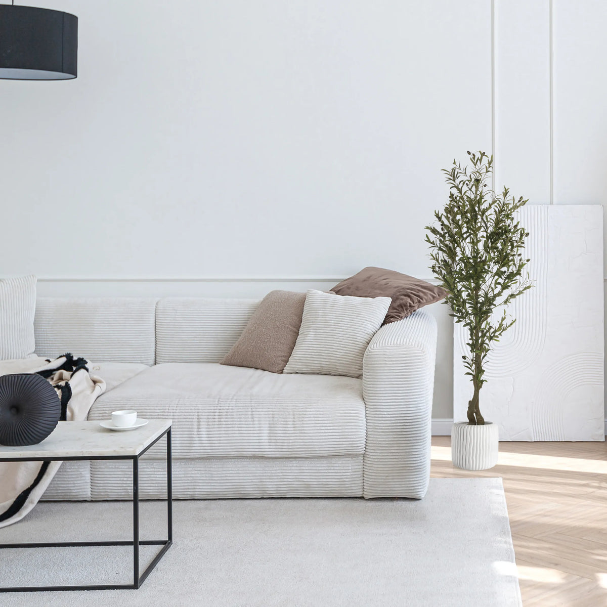 Grön konstgjord växt OLIVE I i en vit kruka bredvid en ljus soffa från hjh OFFICE