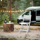 Vit TRAVANO utomhusstol i en skogsmiljö bredvid en husbil från hjh LIVING (AI-genererad bild)
