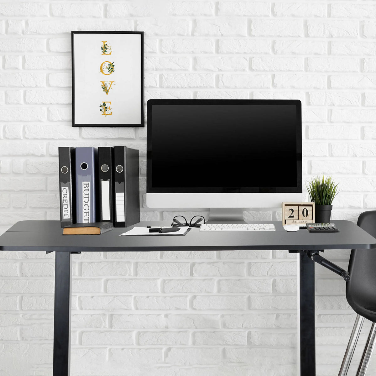 Svart ståskrivbord STAND CR med skärm, tangentbord och pärmar framför en vit tegelvägg från hjh OFFICE