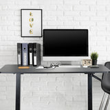 Svart ståskrivbord STAND CR med skärm, tangentbord och pärmar framför en vit tegelvägg från hjh OFFICE