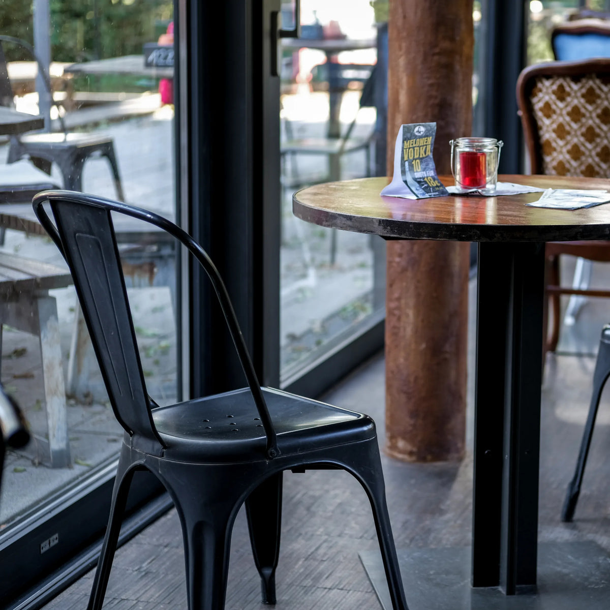 Svart Bistrostol VANTAGGIO BRUSH med svängd ryggstöd vid ett runt bord från hjh OFFICE