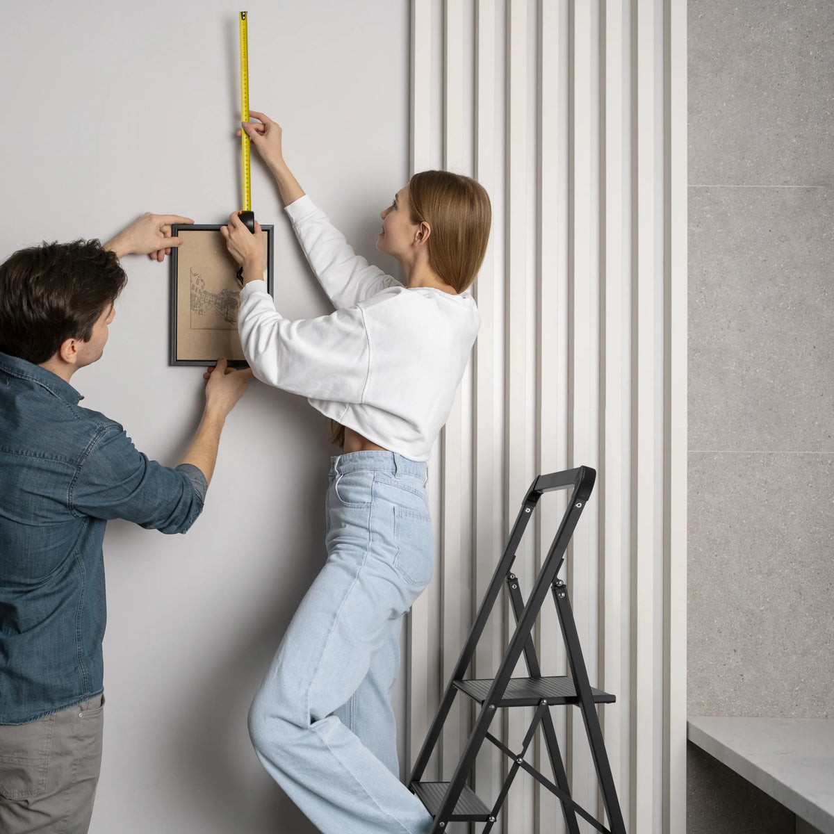 Svart fällbar stege SOLID W6 med tre steg som används vid upphängning av en tavla från hjh OFFICE