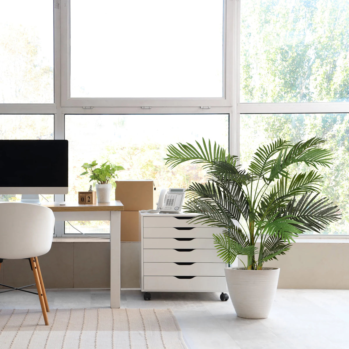 Grüne Kunstpflanze ARECA II in einem weißen Übertopf neben einem weißen Rollcontainer von hjh OFFICE