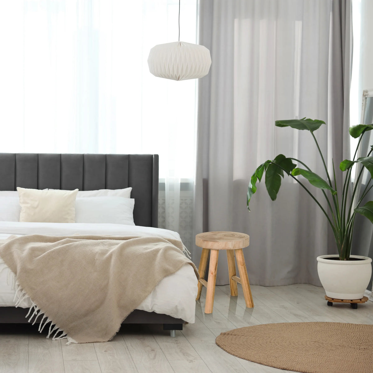 Brun sittpall RUSTIKO W i trä med tre ben bredvid en säng från hjh LIVING